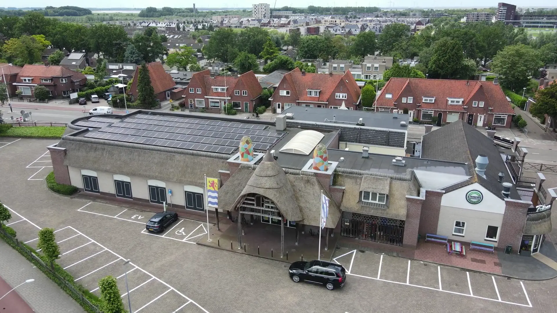 Luchtfoto van een horecabedrijf met zonnepanelen op het dak en een parkeerterrein ervoor